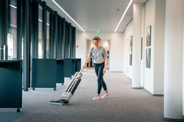 Frau reinigt Bürofläche mit einem Staubsauger